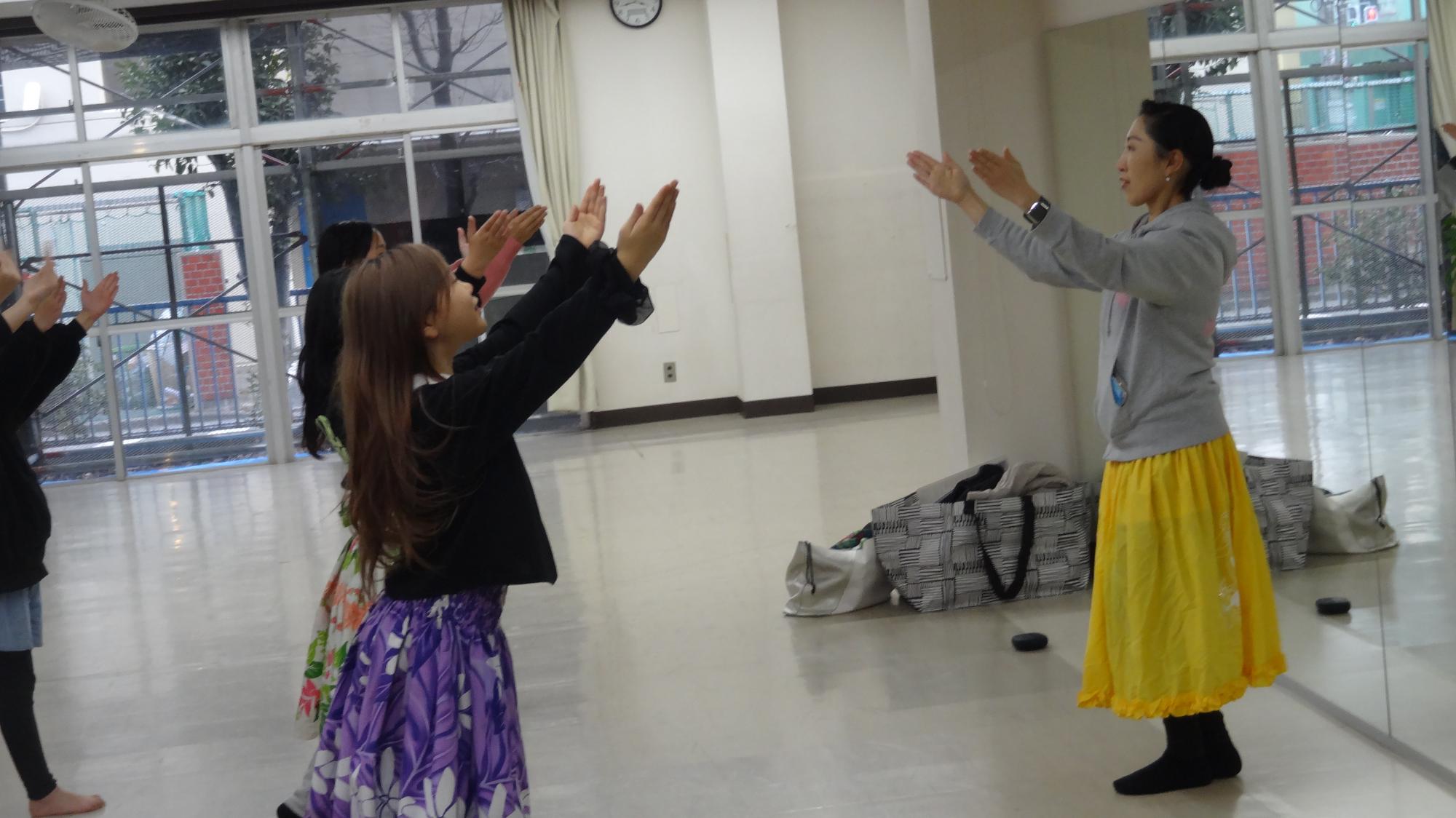フラダンスをしている小学生が先生からポーズを指導されている様子。