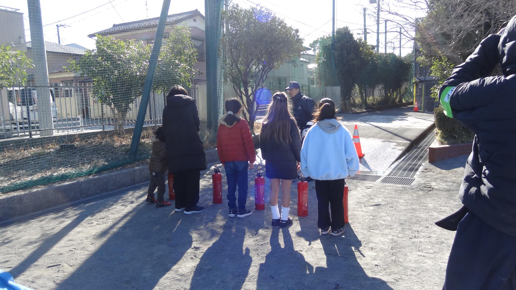 小学生が横に並んで消防士の人の話を聞いている様子