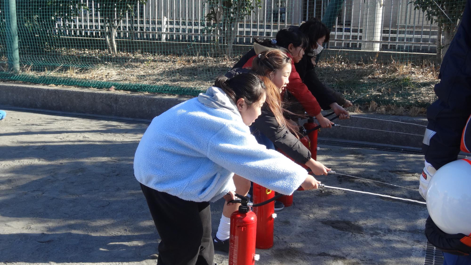 小学生が横に並んで、消火器を体験している様子