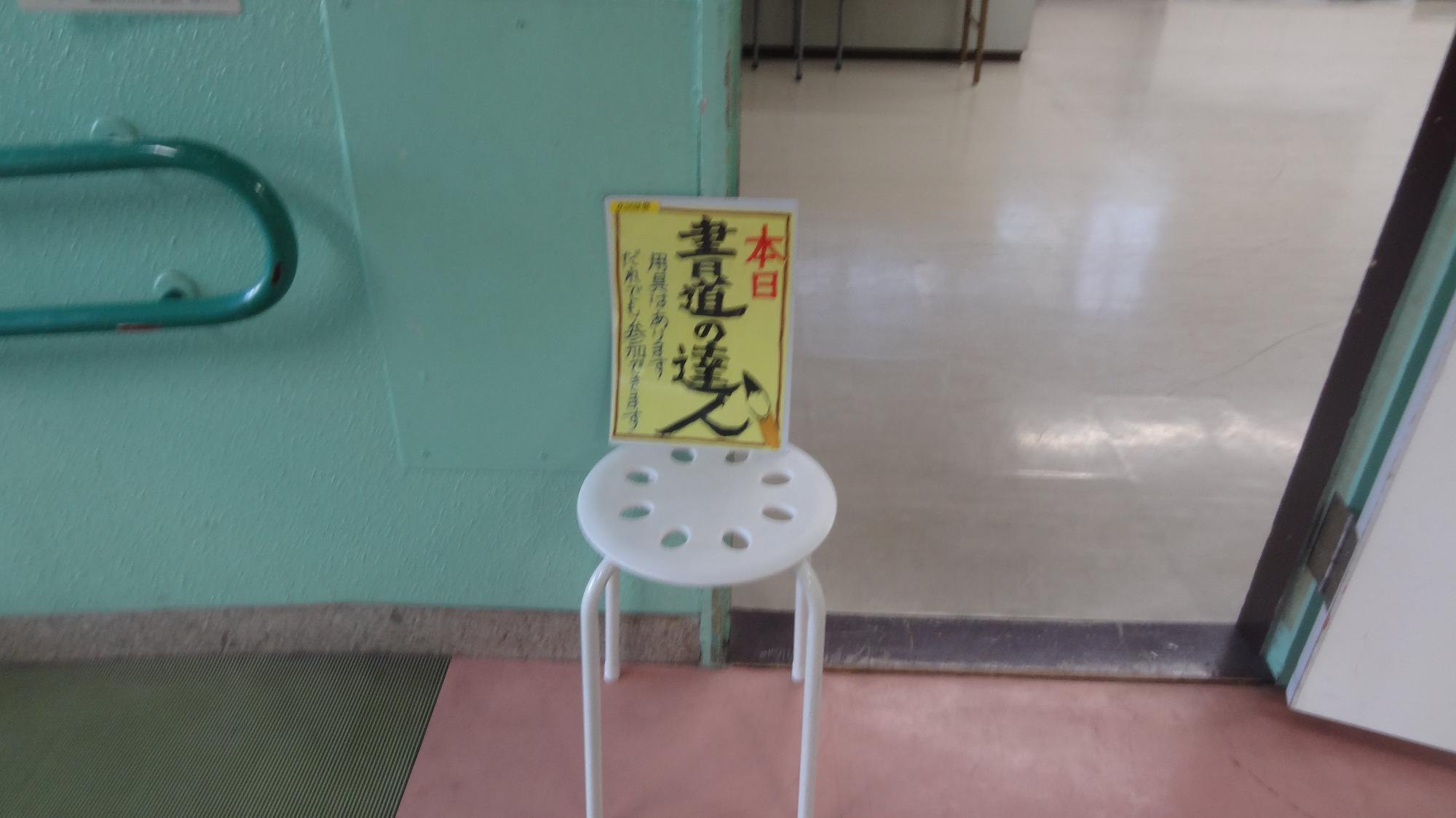 書道の達人と書かれたポスターが小さい丸イスに置かれている写真