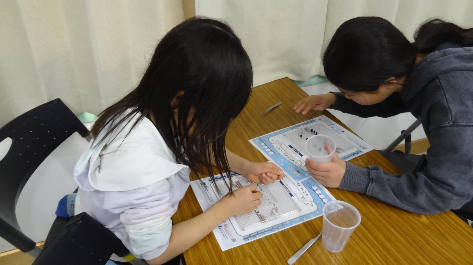小学生二人がアイロンビーズのビーズを並べている様子