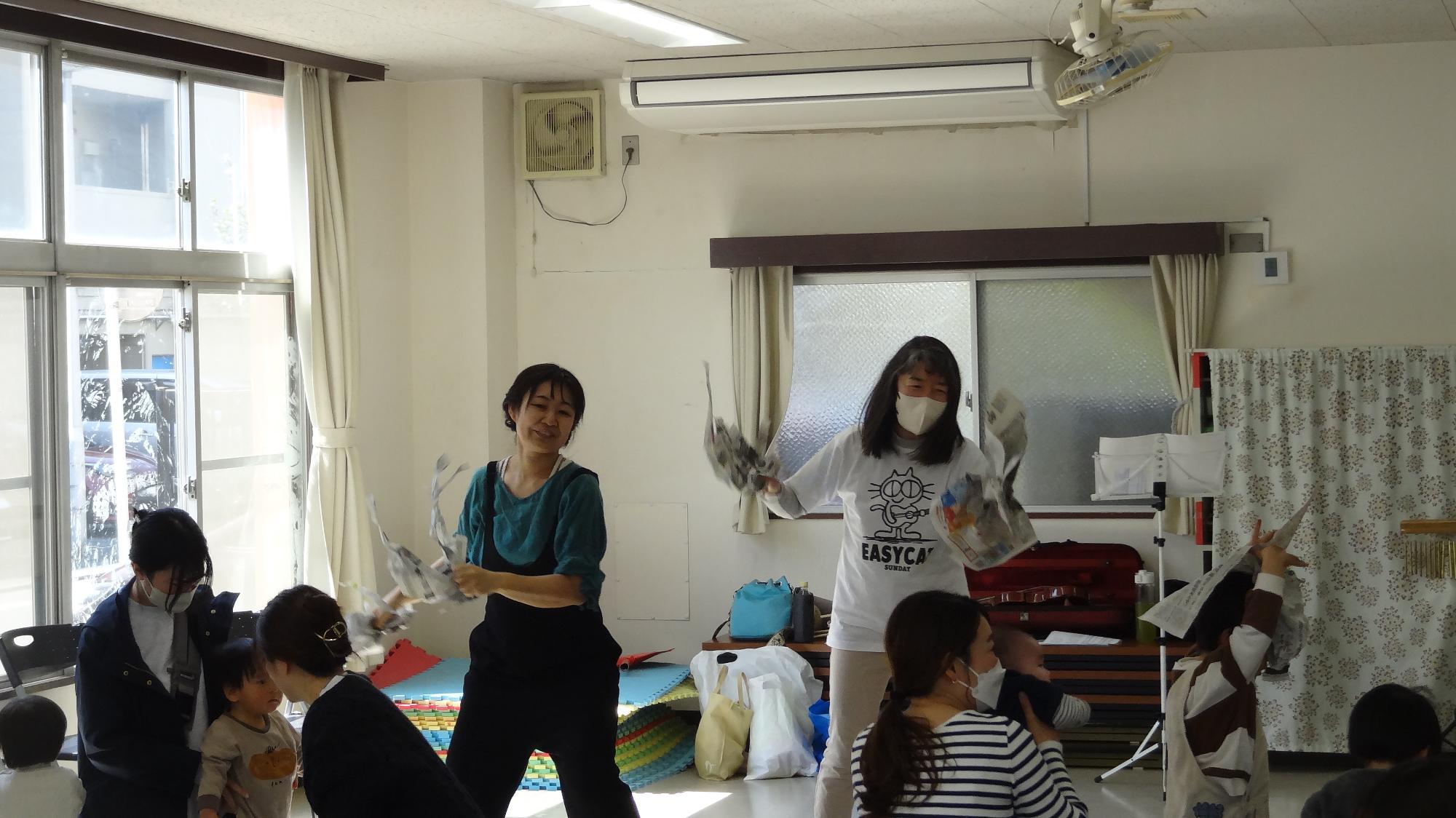 新聞紙を持って女性二人が踊っている様子