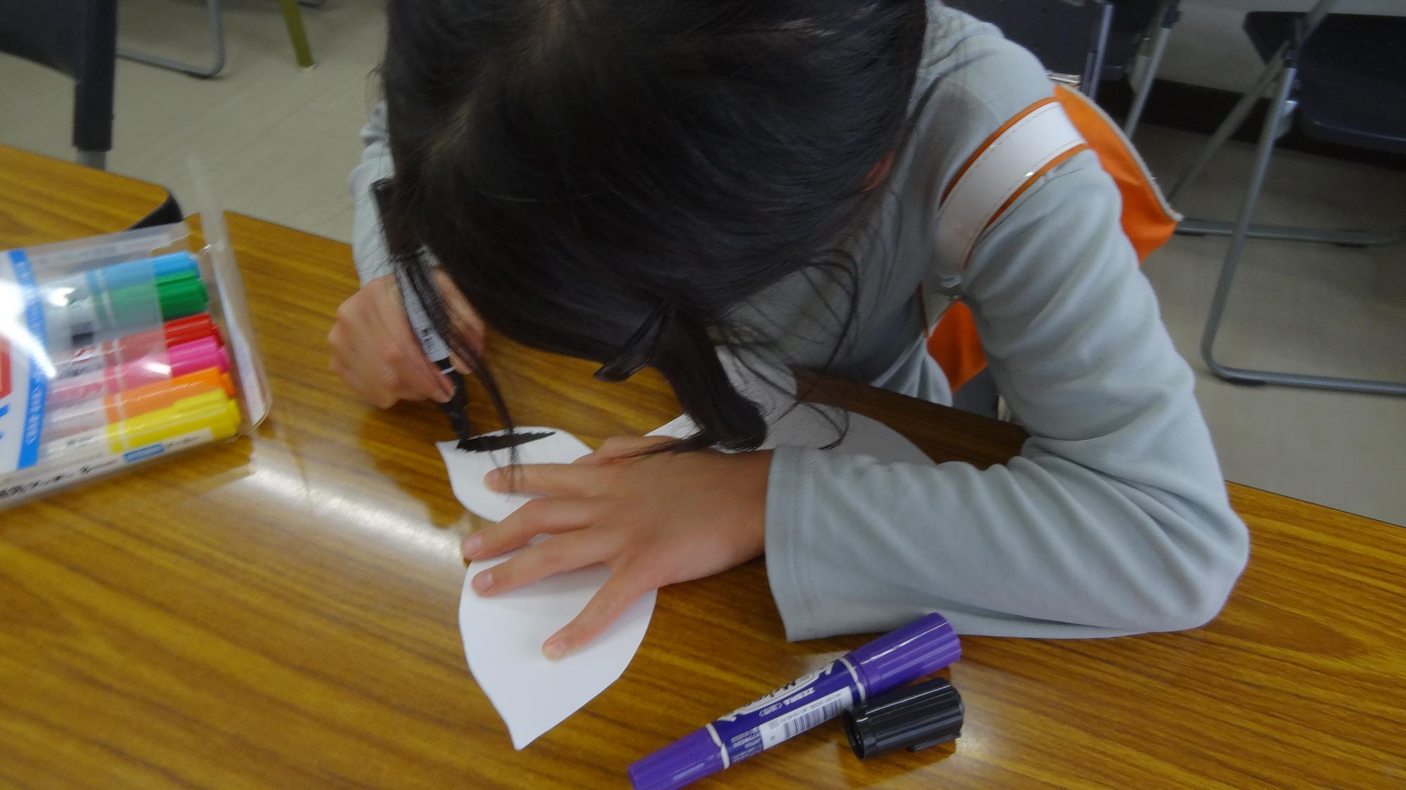 小学生が蝶の形の画用紙に色を付けている様子