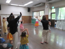 手を広げて楽しそうに踊る親子と講師を撮った写真