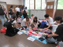マットの上に置かれたベビー服を選んでいる父親と母親たちの写真