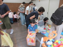 遊具が沢山置いてあるコーナーでしゃがんでおもちゃを選んでいる母親たちの写真