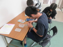 男子中学生3人が手元に集中してクリップを黙々と繋いでいる写真