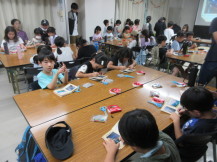 机に並べた本を見ながら絵を描き黙々と制作をする大勢の子供たちを全体的に撮影した写真