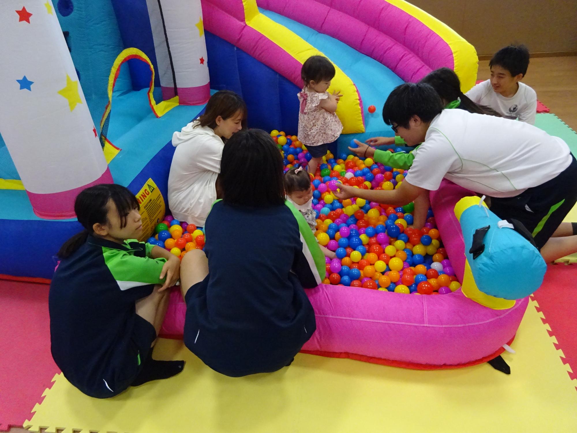 大型遊具のボールプールで遊んでいる乳幼児親子と中学生の写真