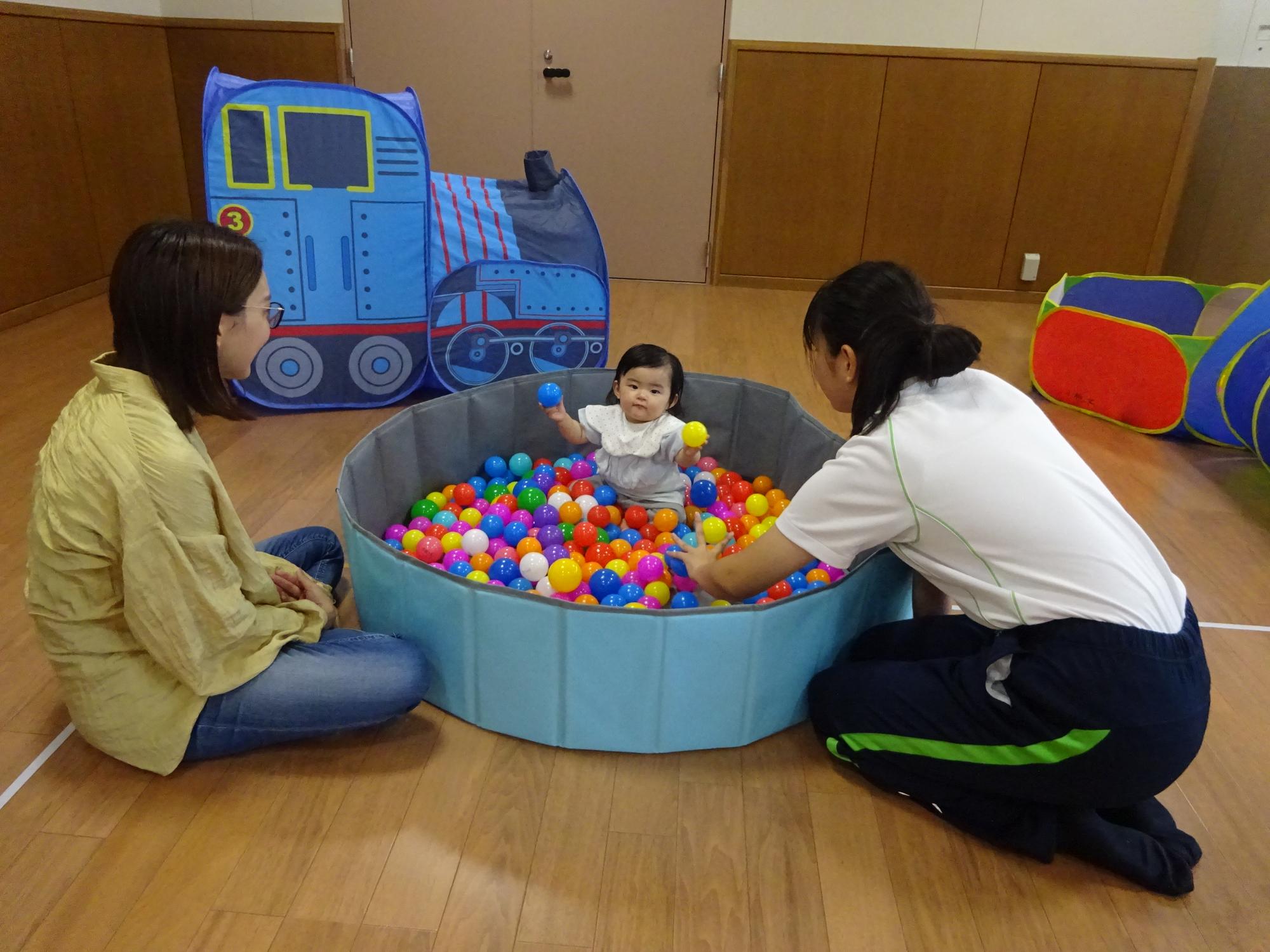 大型遊具のボールプールで遊んでいる乳幼児親子の写真