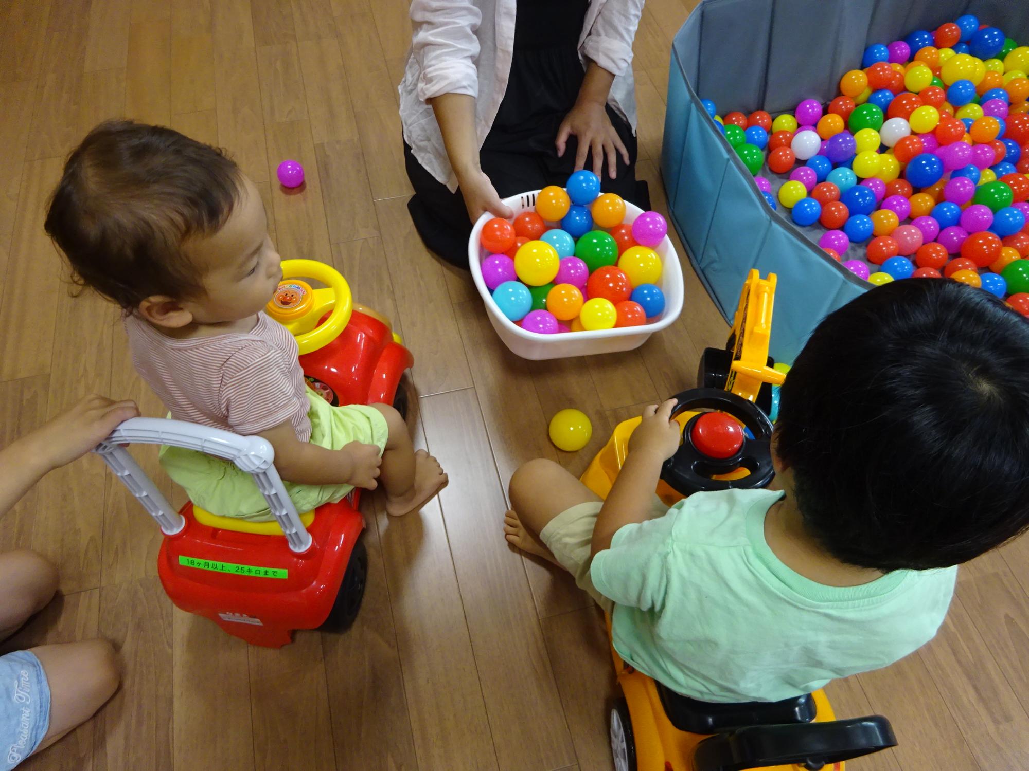 コンビカーに乗ってカラーボールをすくって遊ぶ幼児の写真