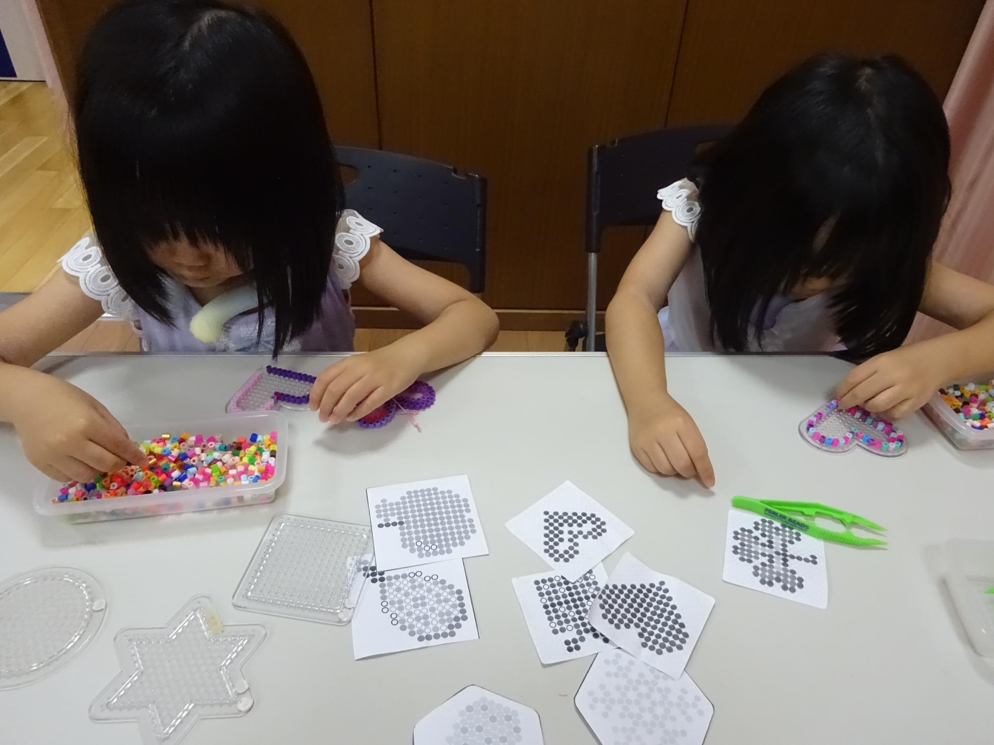 真剣にハート型のビーズを作る双子の女の子の写真
