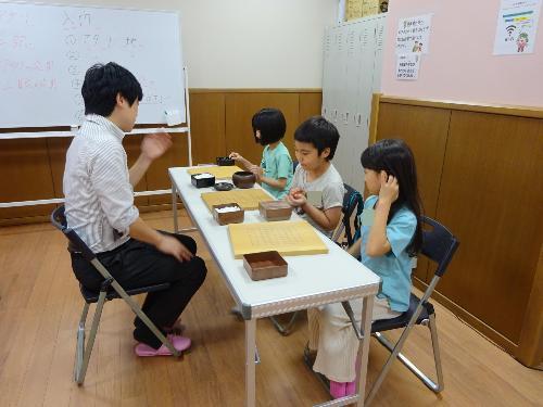 碁盤の前で講師の説明を聞いている3人の小学生の写真