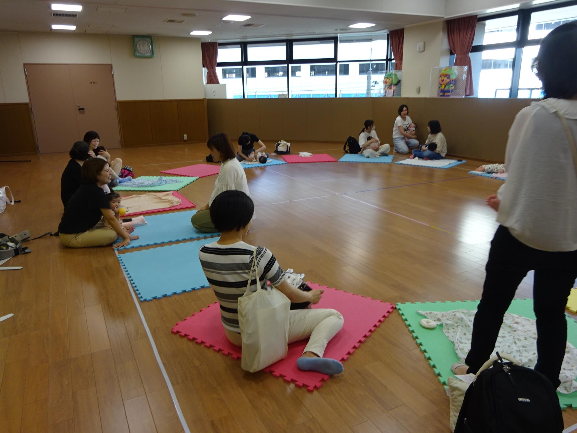 マットの上で談笑している乳児親子の写真