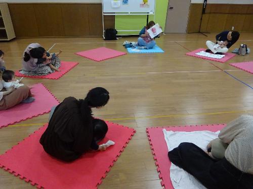 だるまの絵に合わせて身体を動かしている乳児親子の写真