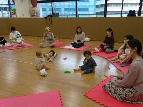 マットの上で談笑する乳児親子の写真