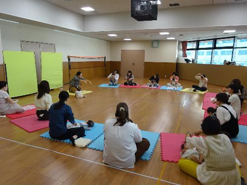 カラフルなマットの上で講師の話を聞く幼児親子たちの写真