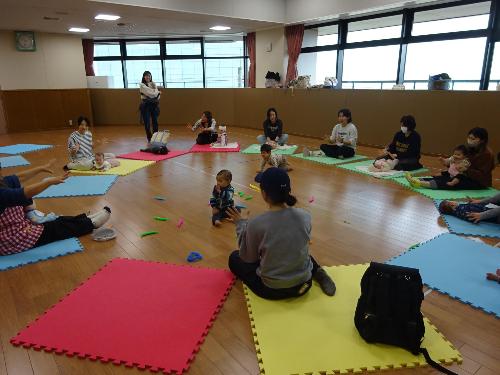 カラフルなマットの上で手遊びをする幼児親子たちの写真