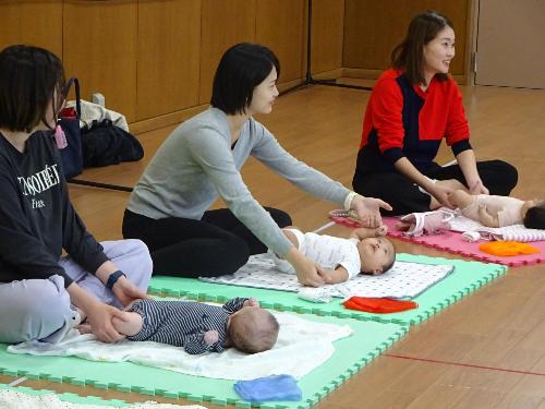 カラフルなマットの上でベビーマッサージをしている3組の親子の写真