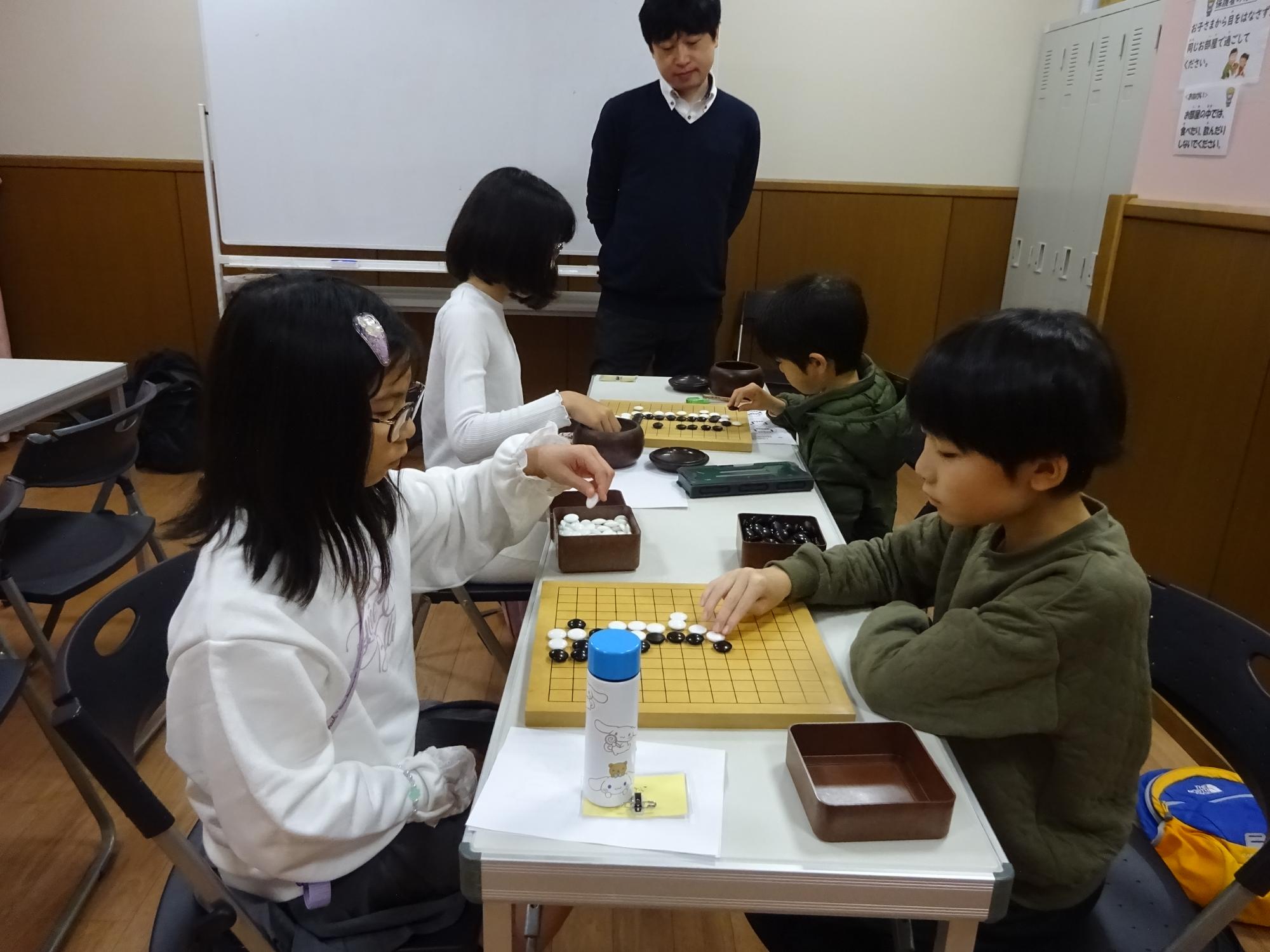 対局をしている4人の小学生と講師の写真