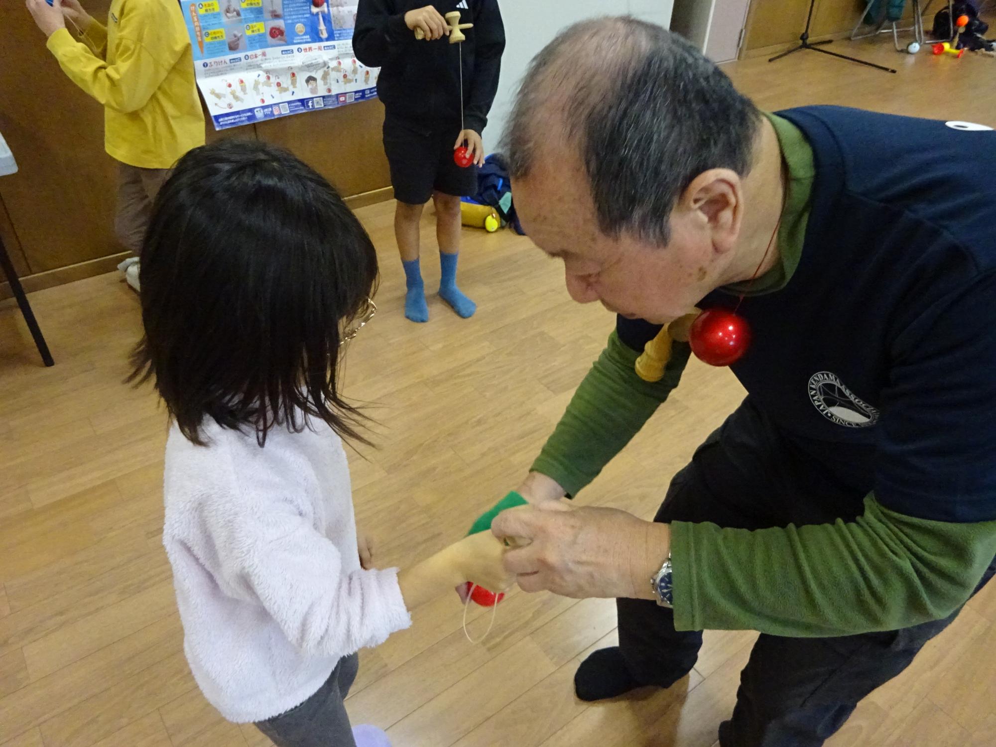 講師に丁寧にけん玉の技を教えてもらっている様子