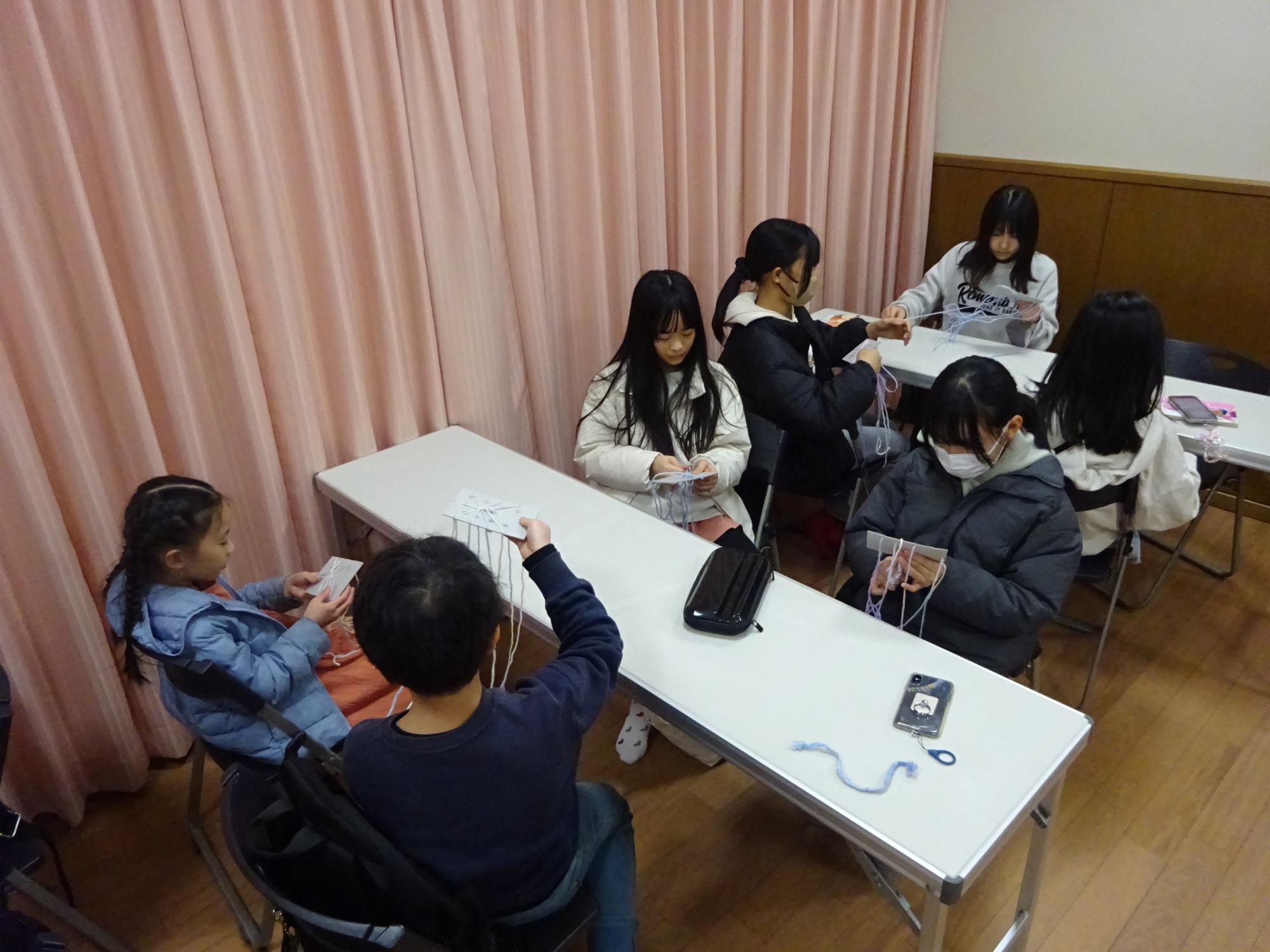 友達と話をしながら糸でミサンガを編んでいる様子