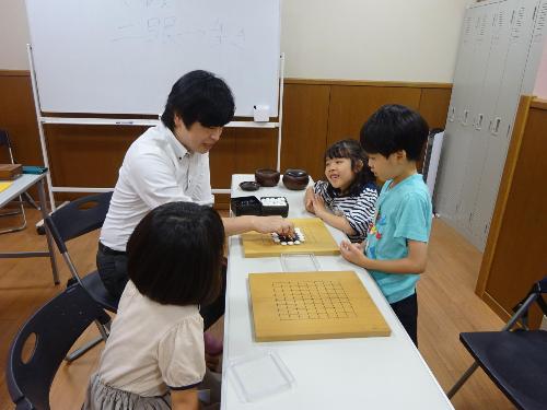 碁盤を前に講師の説明を聞いている子どもたちの写真