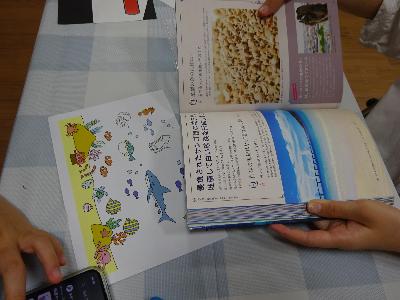 海に関する本を見ながらどんな絵を描くか考えている子どもの写真