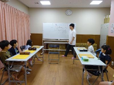 碁盤を前に講師の説明を聞いている子どもたちの写真