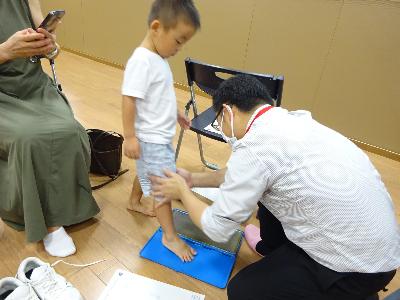 足型の確認をするためにインクに足をつけている子どもと補助をする講師の写真
