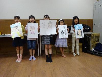 自分で書いた自画像を手に持って記念撮影をしている子どもたちの写真