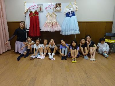 バレエの衣装の前で記念撮影をする講師と子どもたちの写真