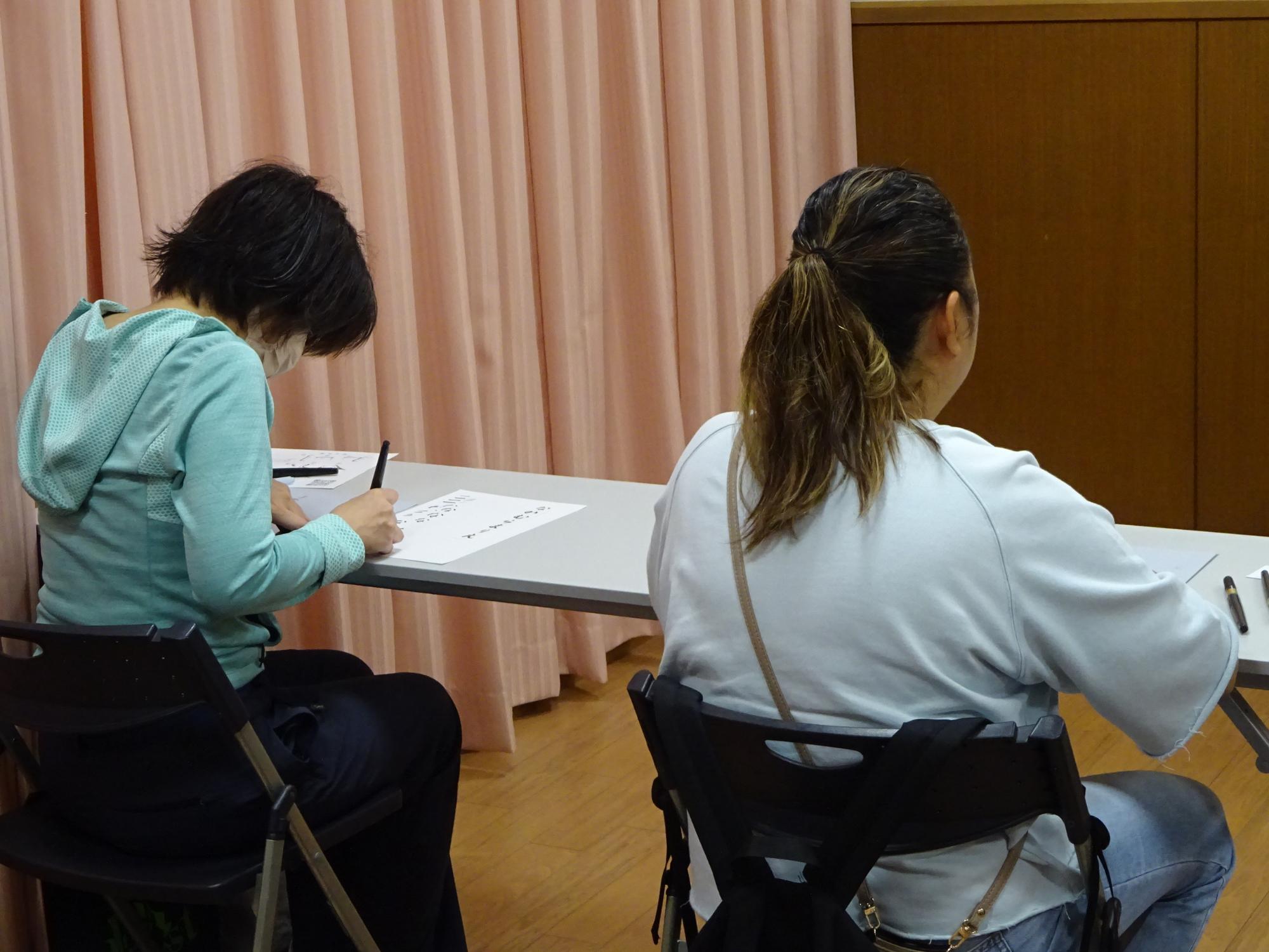 筆で文字を書く練習をしている参加者たちの写真