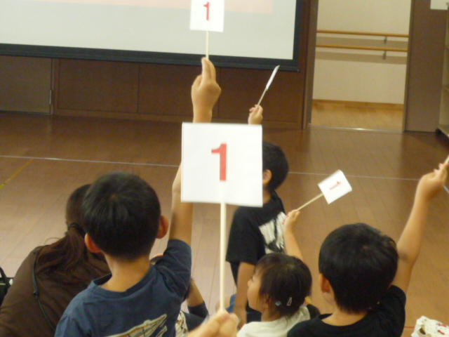 クイズの回答番号の札を上げる参加者たちの写真