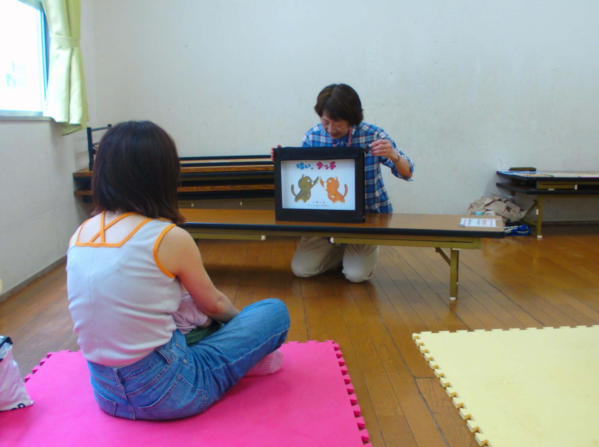 乳幼児親子が紙芝居の読み聞かせを見ている写真