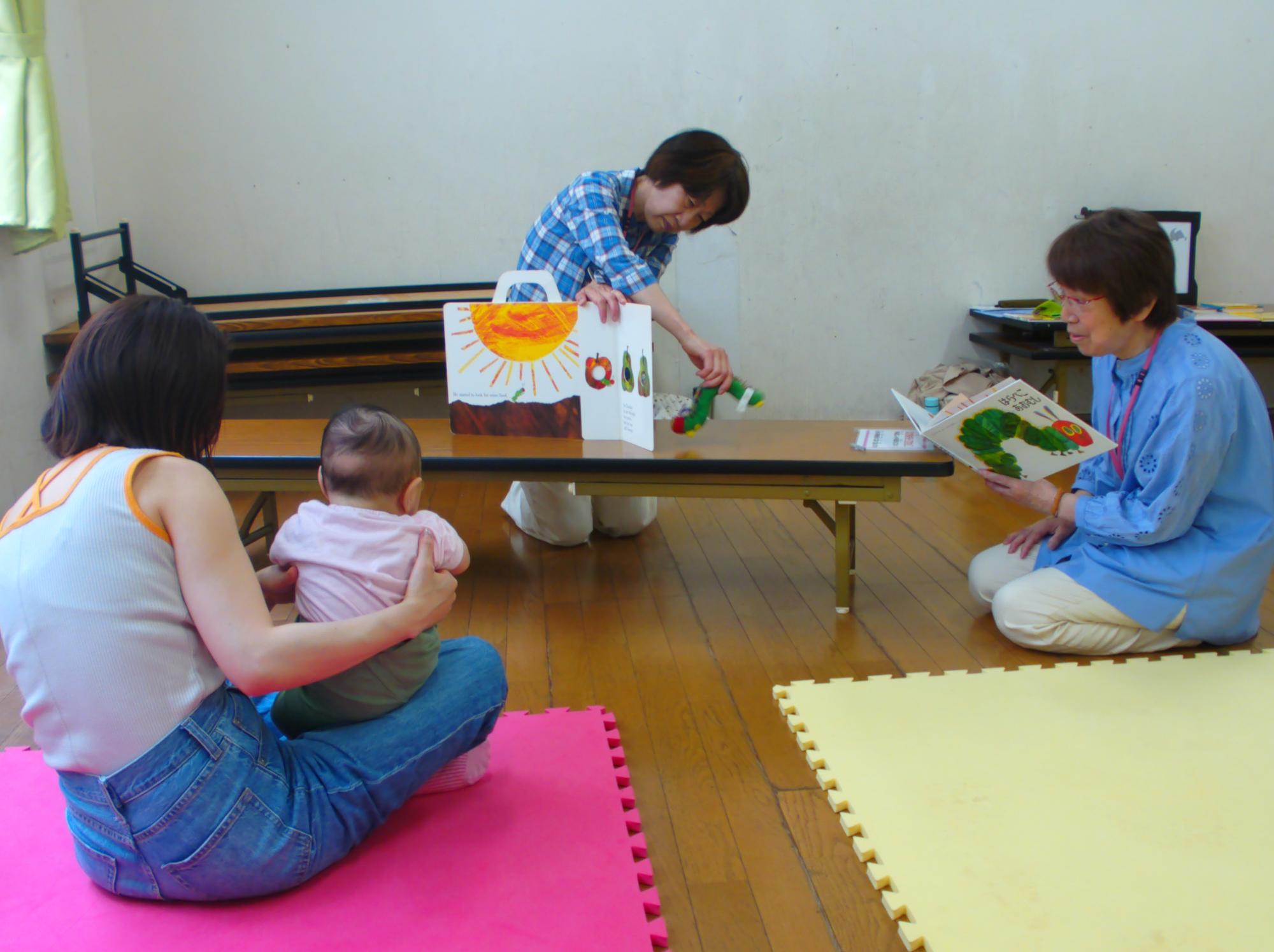 乳幼児親子が人形を使った大型絵本の読み聞かせを見ている写真