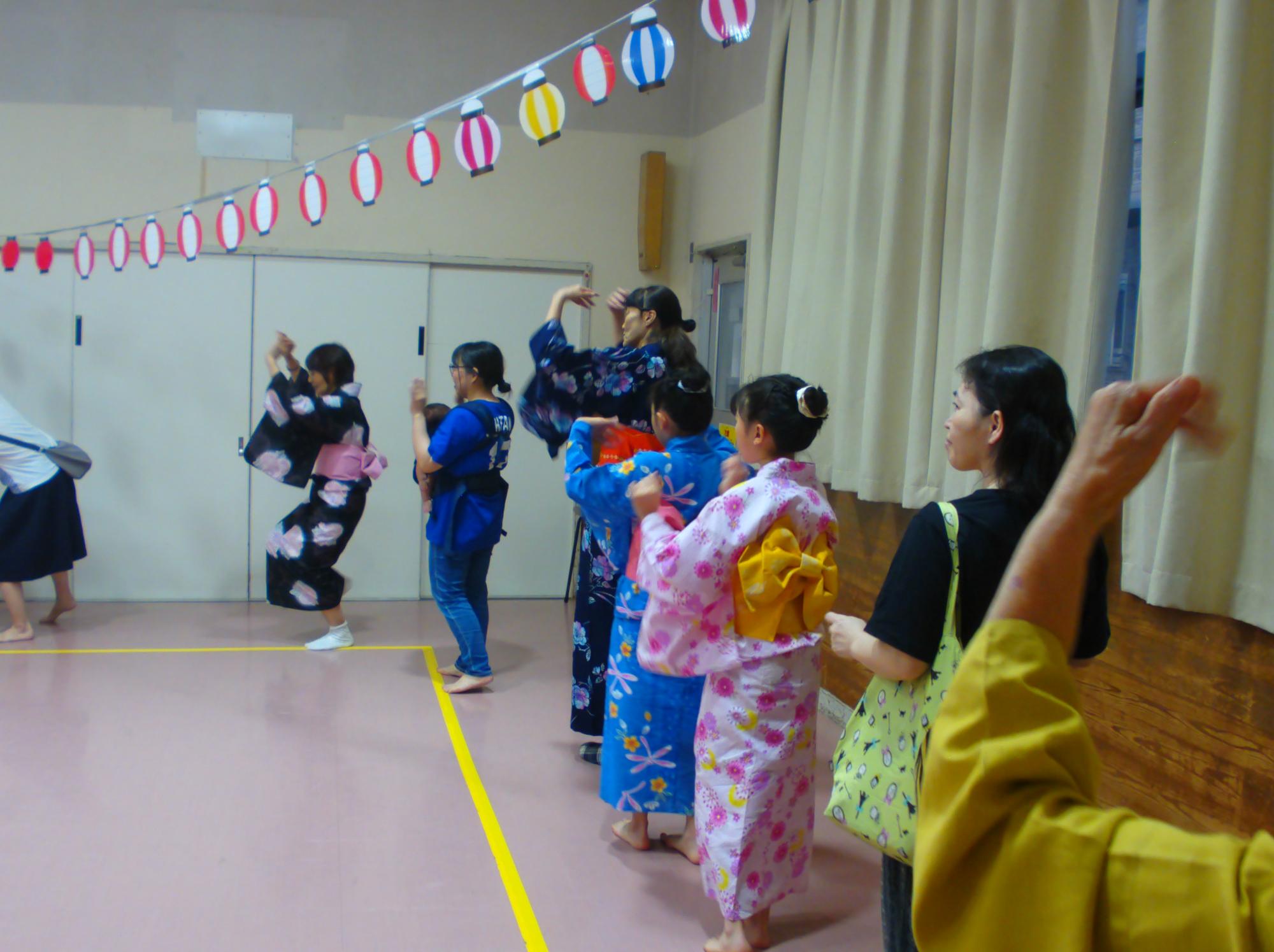 集会室で円になりながら、盆踊りを踊っている写真