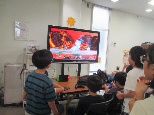 後ろから立ってゲームを観戦する子どもたち