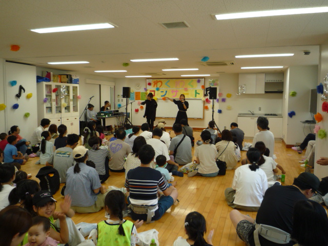 沢山の参加者が座っており、ステージに2人のアーティストが歌やダンスを披露している写真