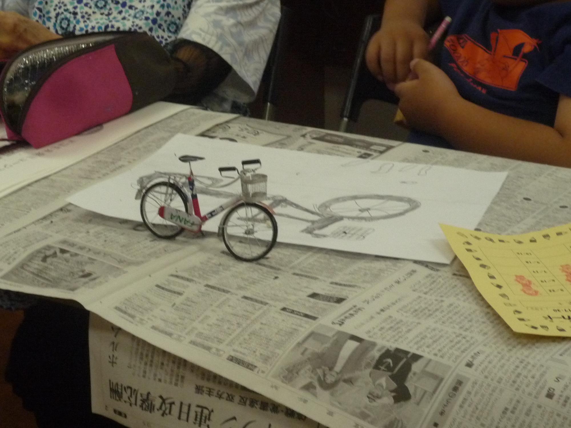 小さい自転車のミニチュアを見ながら絵を描く小学生