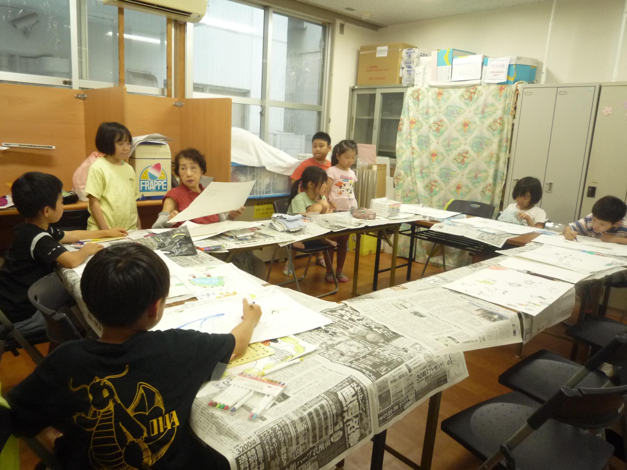 真剣に絵を描く小学生と、先生に相談する小学生