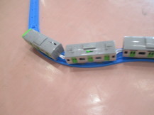 ピンク色の床の室内で、青いプラレールの上を灰色の3両つながった電車の模型が走っている写真