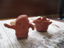 新聞紙の敷かれたテーブルの上に置かれた、茶色の粘土で作られた埴輪と土器の写真