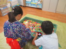 黄緑色のビニールシートが敷かれた部屋の中で、色とりどりのスーパーボールと水の入った緑色のトロ船の前で浴衣を着た子どもたちがスーパーボールすくいをしている写真