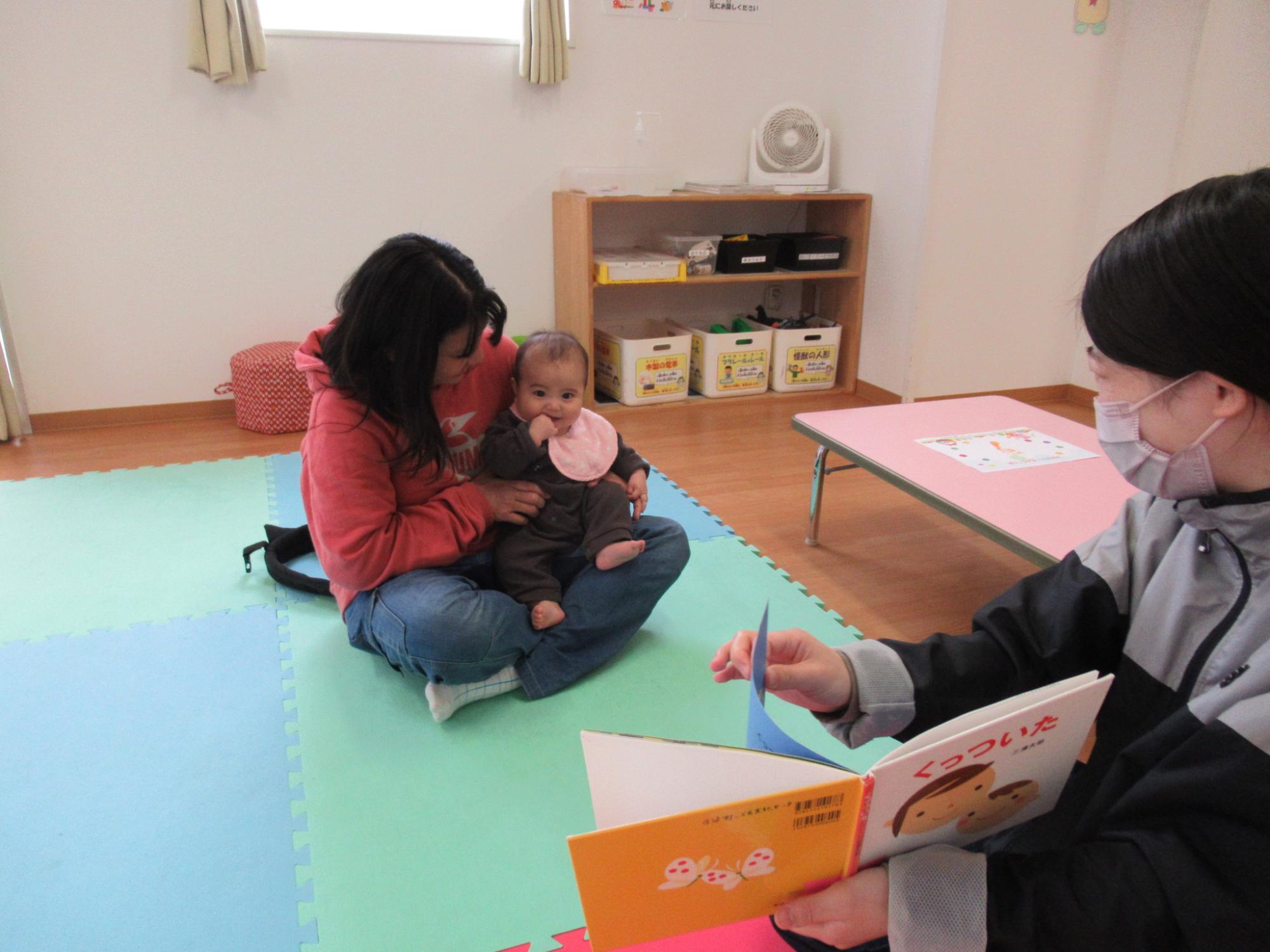 笑顔で絵本の読み聞かせを楽しんでいる0歳児の写真