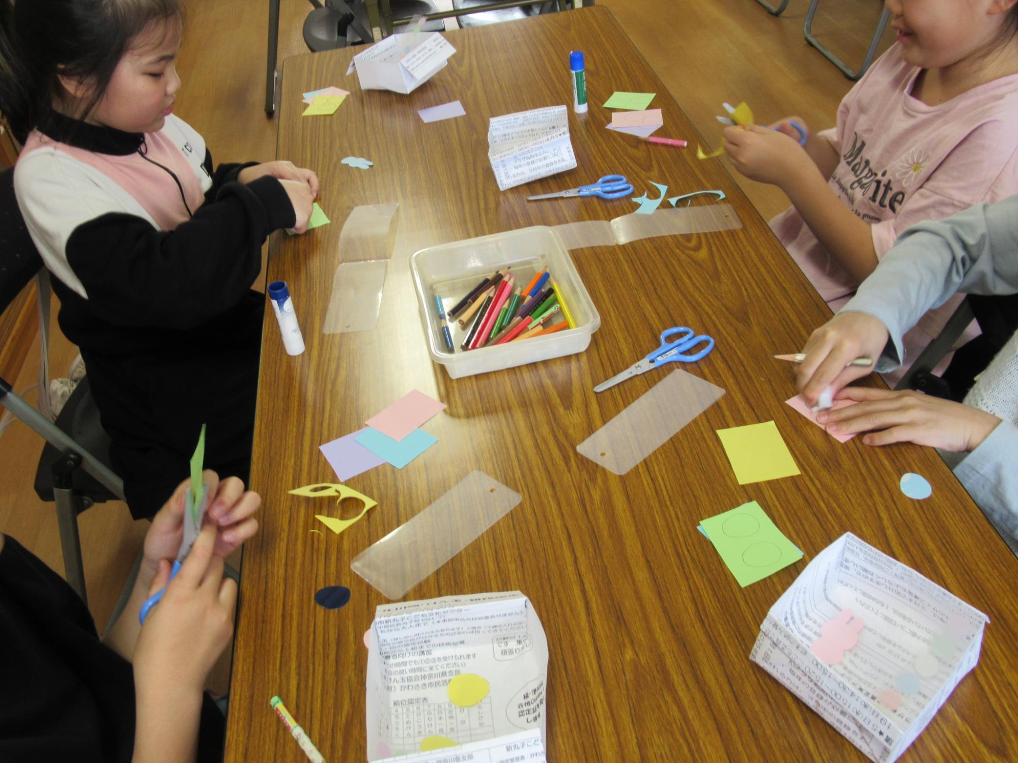 しおり作りにて画用紙を型取り、はさみで切っている子どもたちの写真