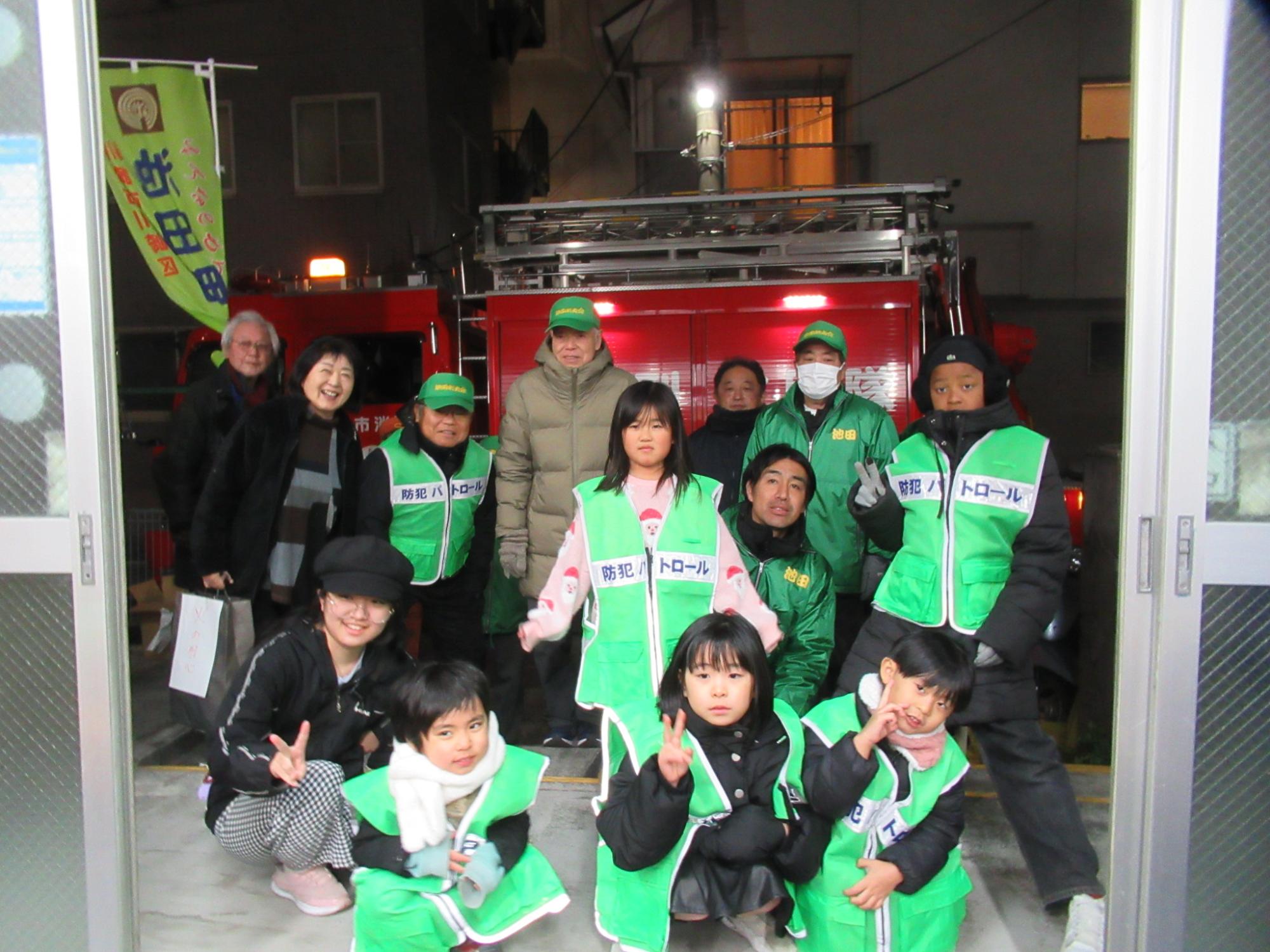 消防車の前でポーズを撮っている子どもたちと成人の写真