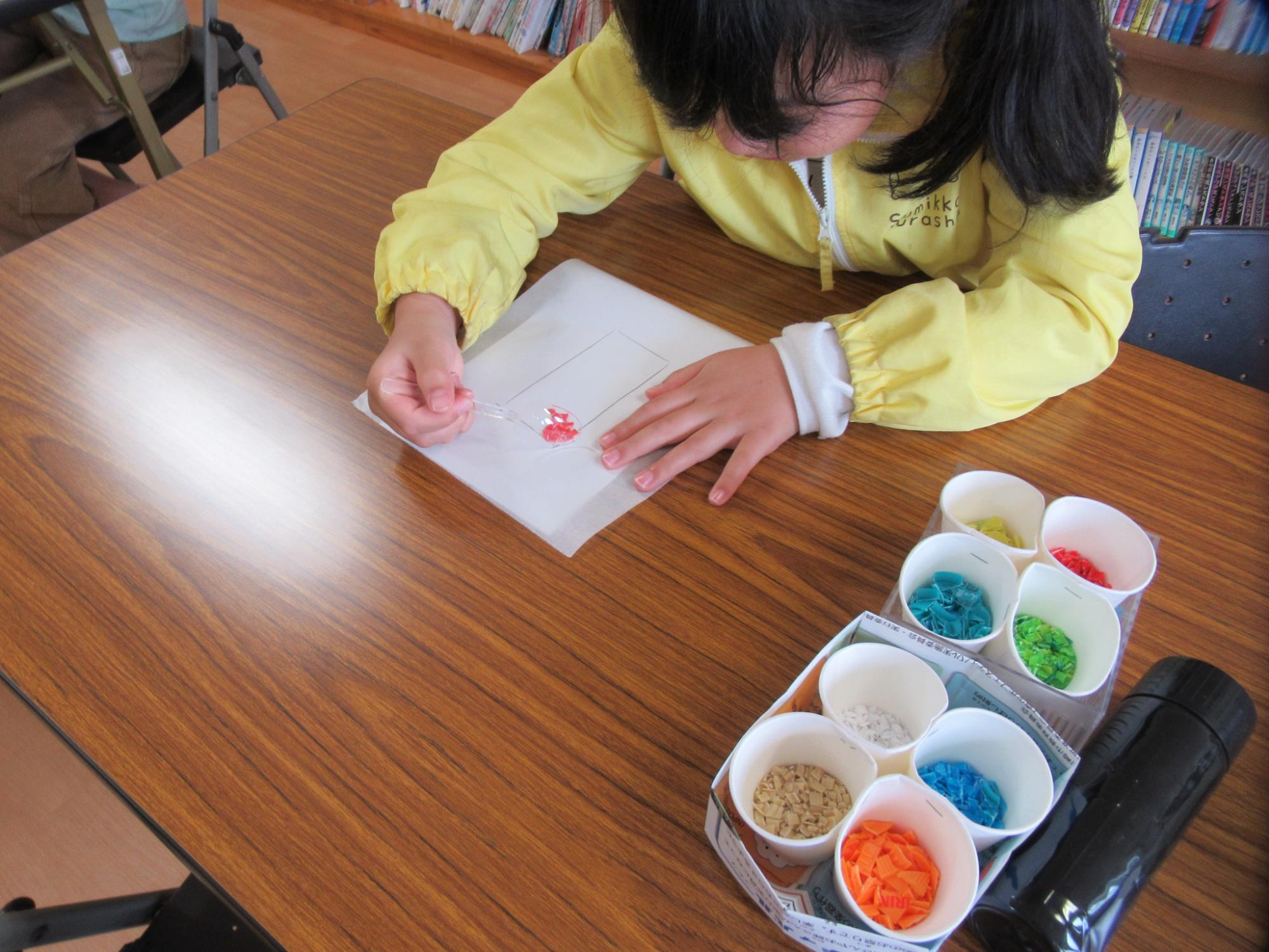細かく切ったプラスチックのキャップをクッキングシートに並べている子どもの写真