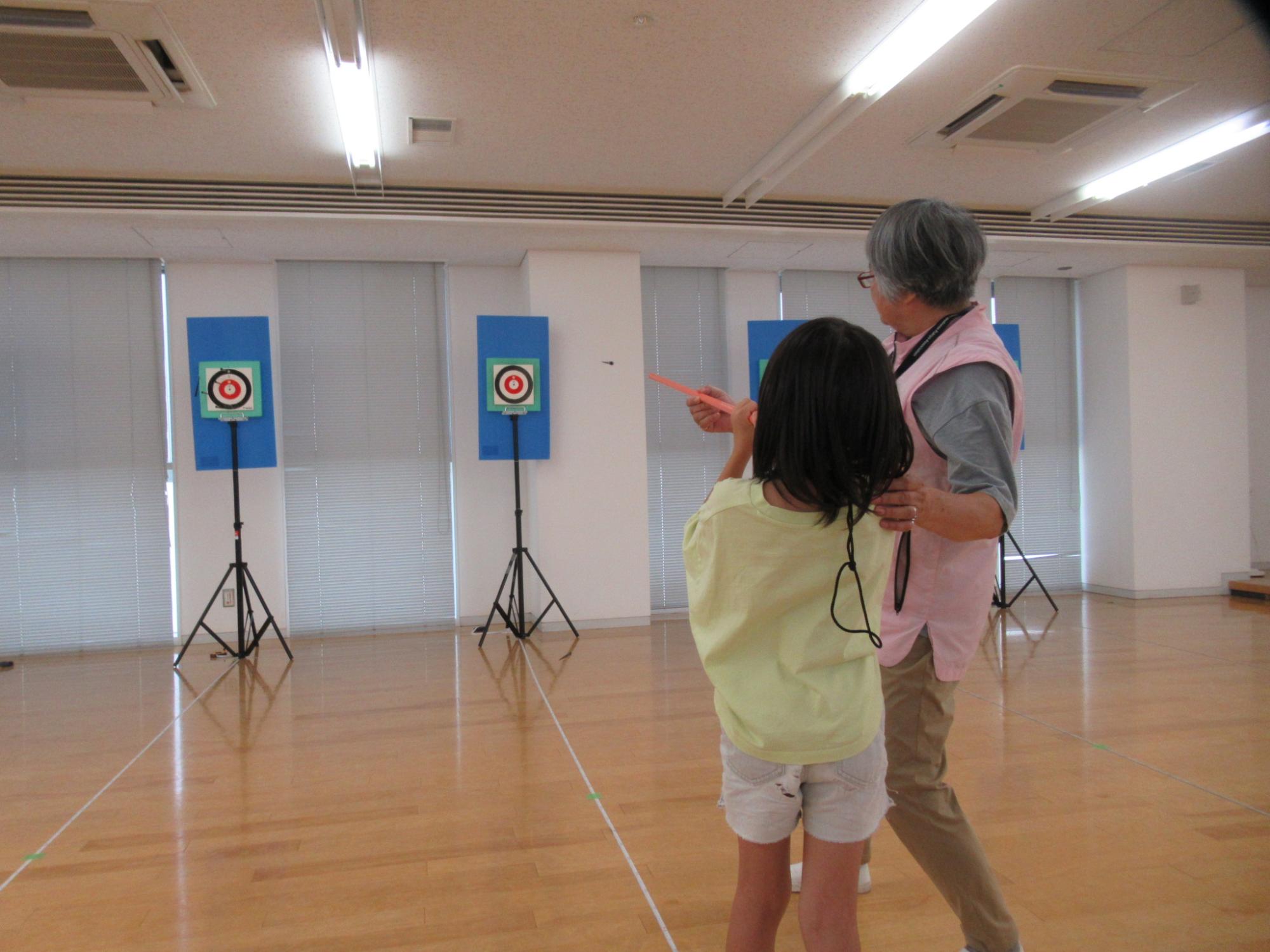 老人に教わりながら吹矢を楽しむ小学生の写真