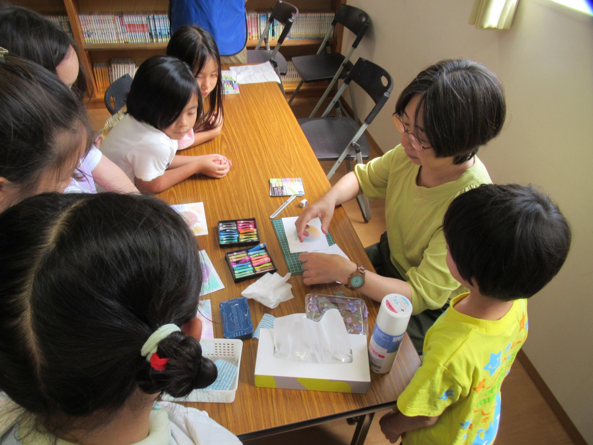 講師によるパステルアートの説明を聞いている子どもたちの写真